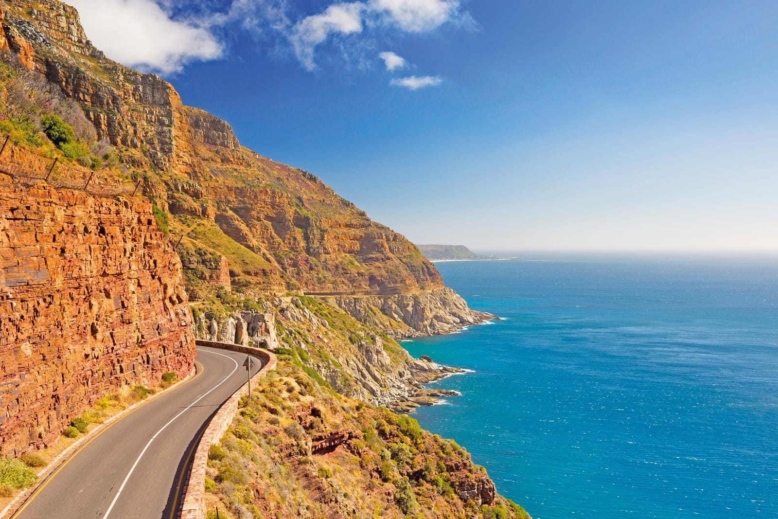 Küstenstraße in Südafrika, felsige Klippen, blaues Meer, sonniger Himmel.