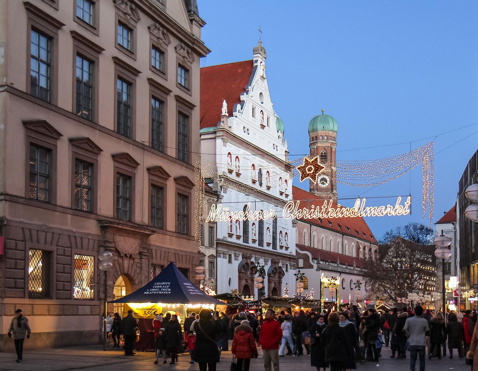 Münchner Christkindlmarkt bei Dämmerung, Lichter und Menschenmengen in festlicher Stimmung.