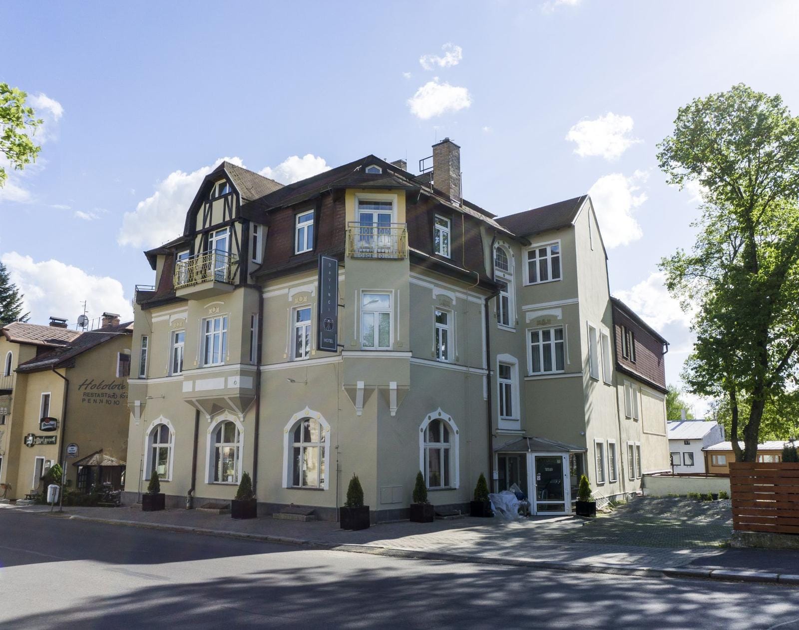 Historisches Hotel im Landhausstil mit großen Fenstern und grüner Fassade, sonnig gelegen.