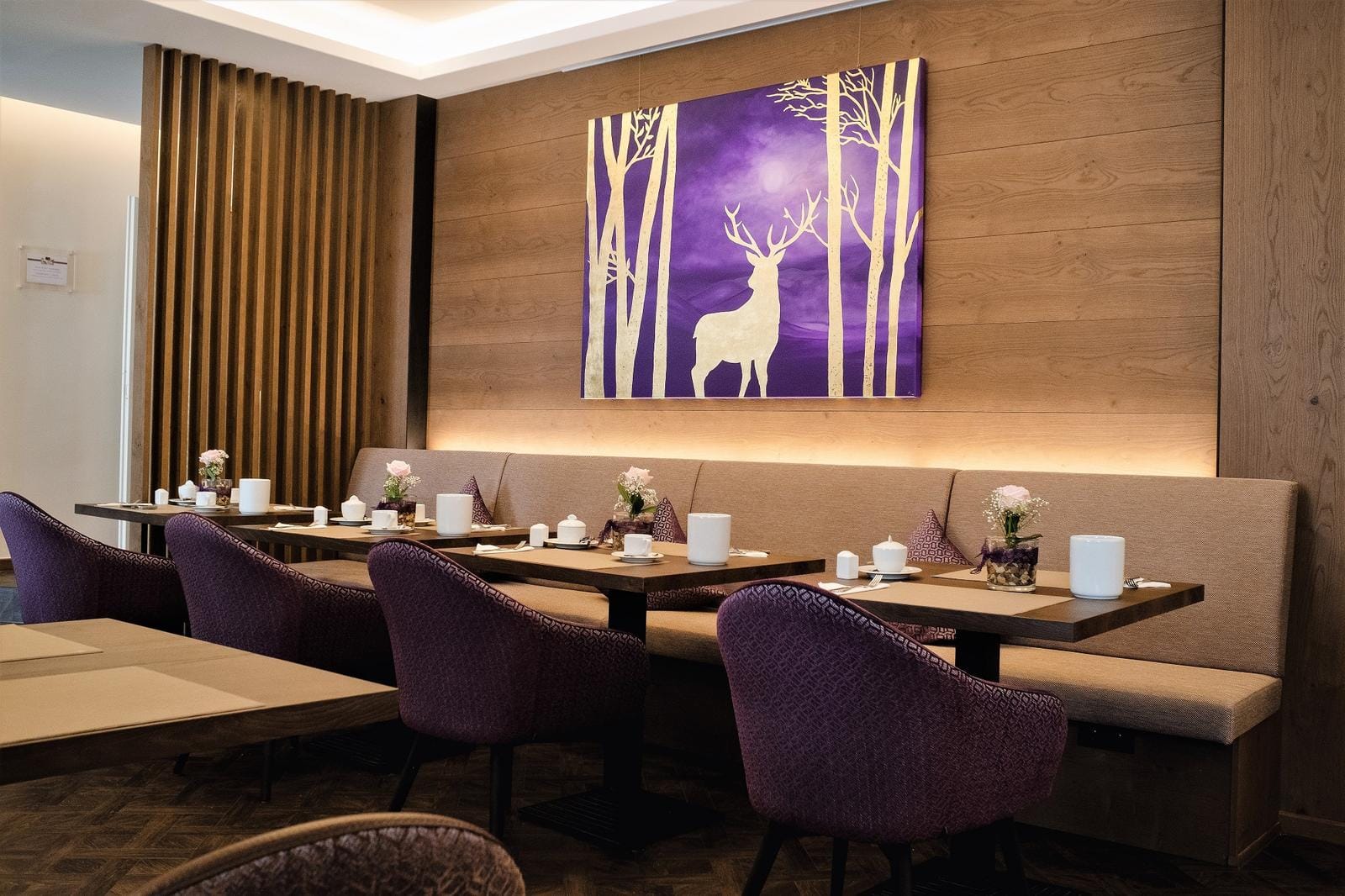 Modernes Hotelrestaurant mit lila Stühlen und Waldgemälde auf Holzwand.