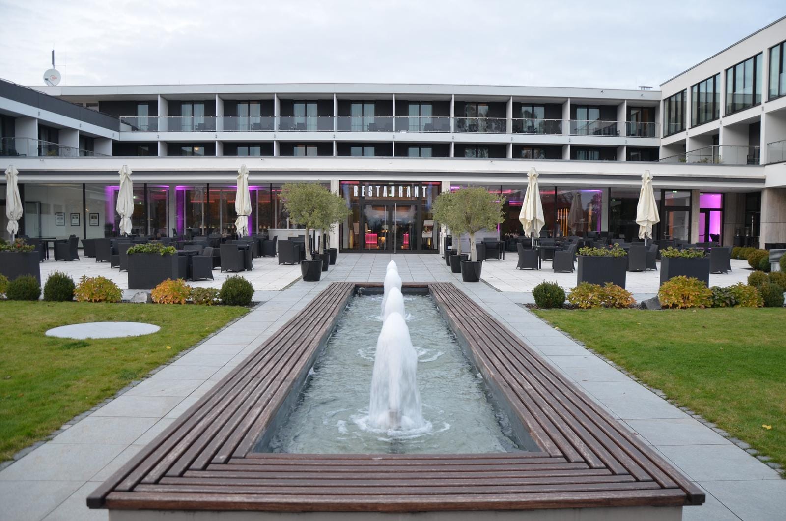 Modernes Hotel mit Außenbereich, lila Beleuchtung, Springbrunnen und eleganter Terrasse.