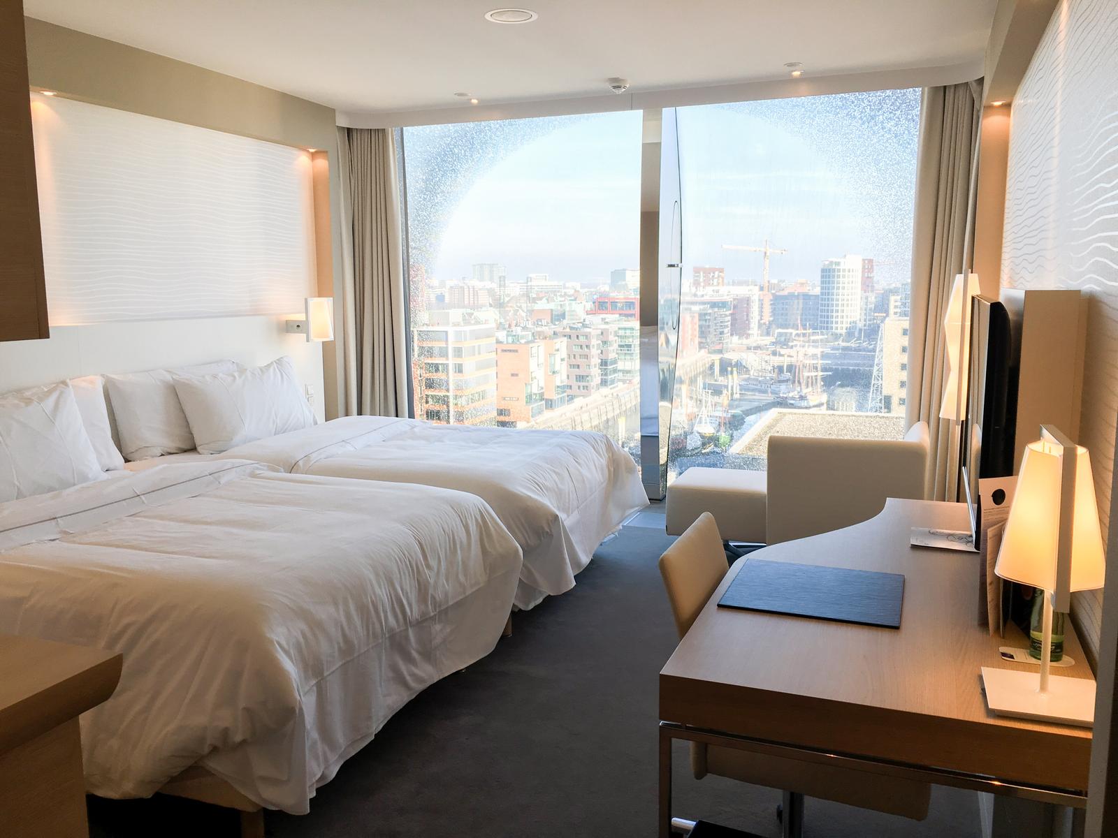 Modernes Hotelzimmer mit Doppelbetten, Schreibtisch und Panoramablick auf die Stadt.
