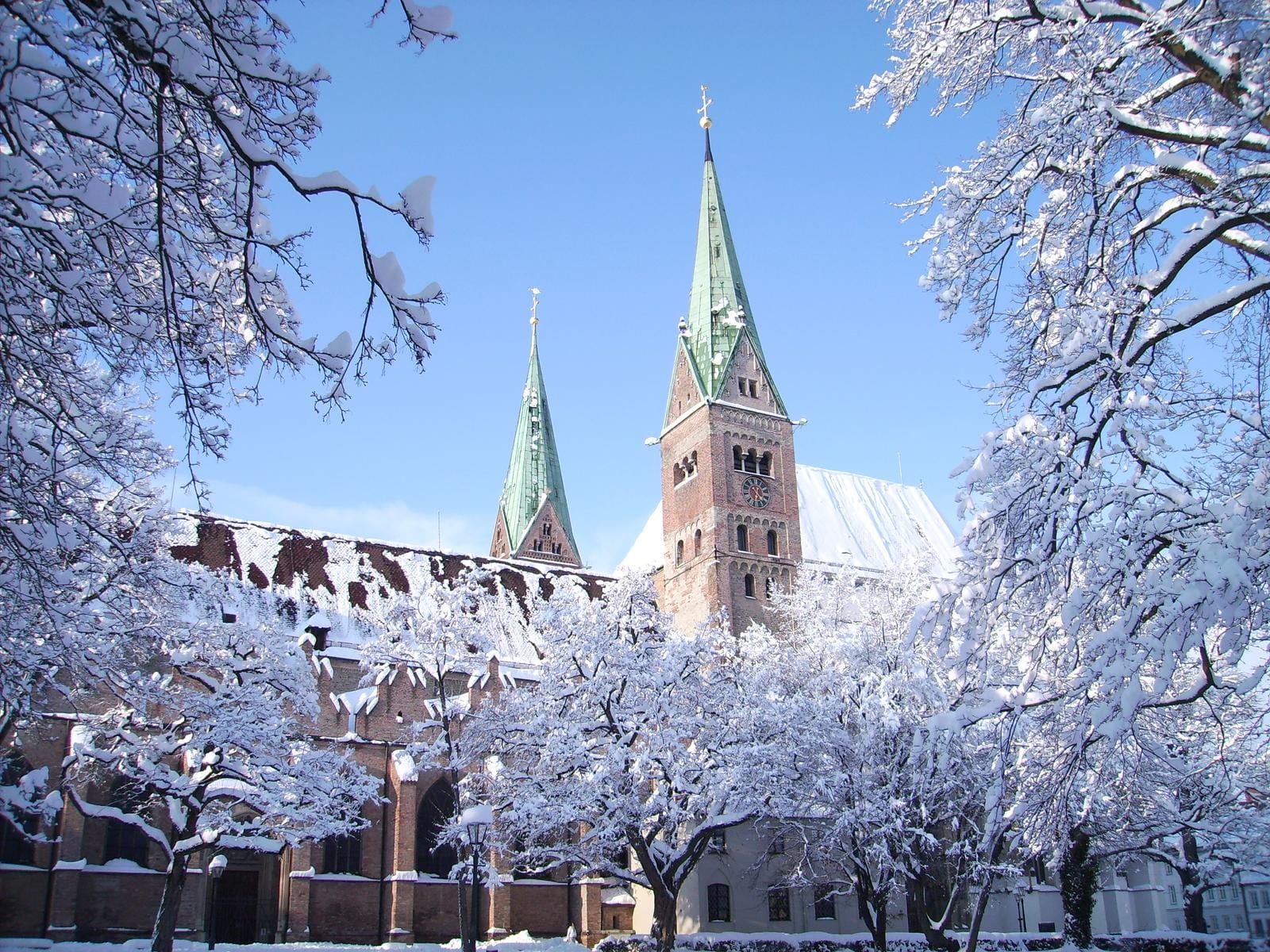 Winterliche Kirche mit schneebedeckten Bäumen und blauem Himmel in Deutschland.