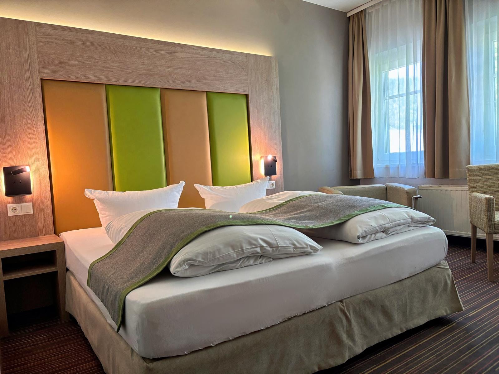 Modernes Hotelzimmer mit Doppelbett, buntem Kopfteil und sanfter Beleuchtung.