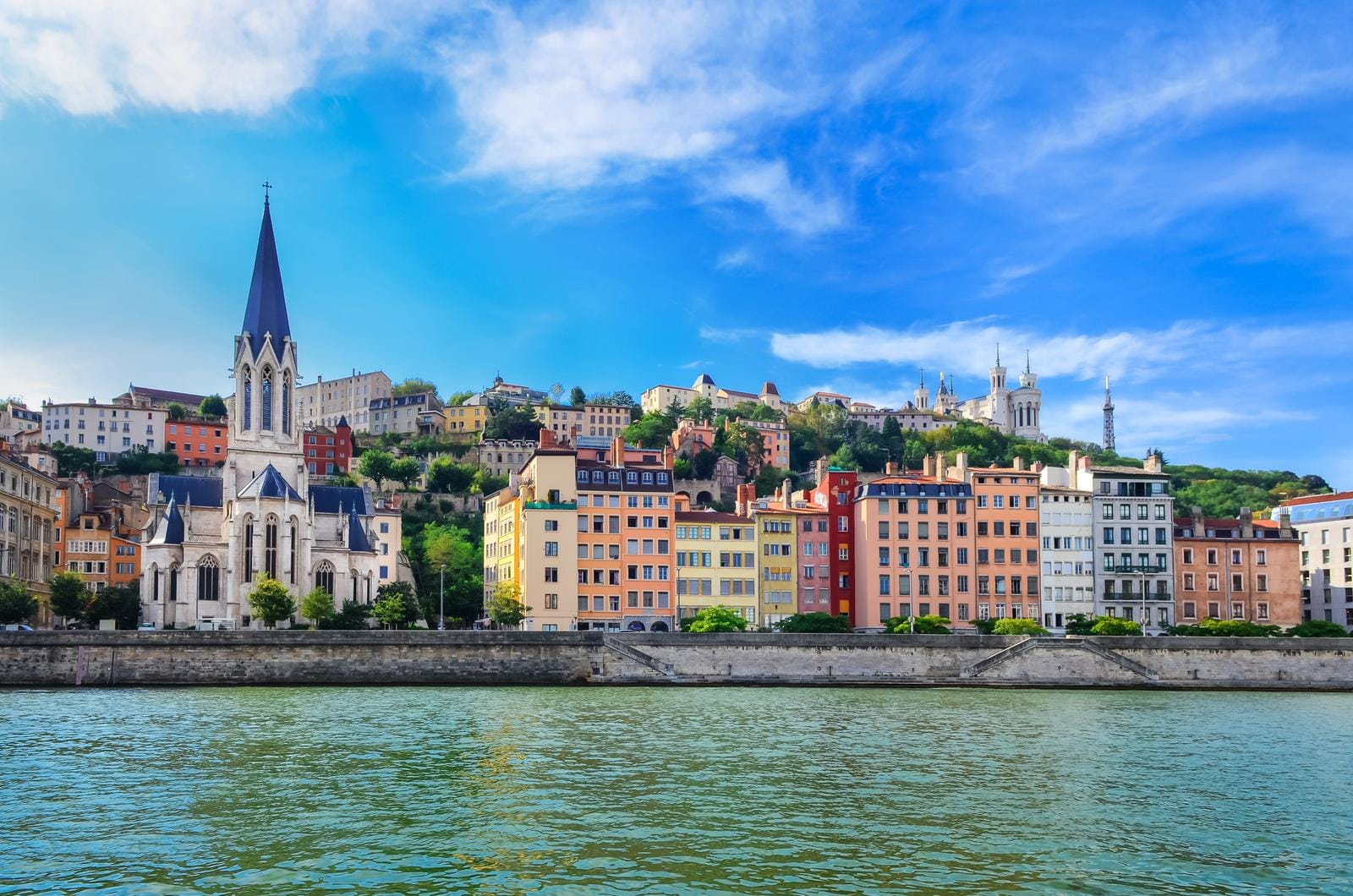 Bunte Gebäude, markante Kirche und grüne Hügel im sonnigen Lyon, Frankreich.