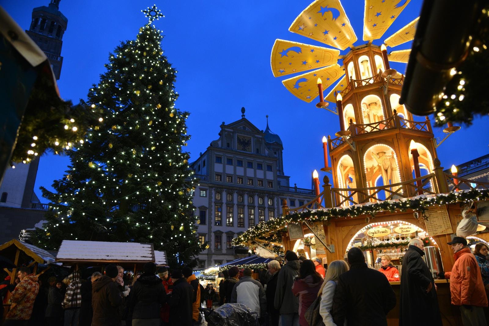 Weihnachtsmarkt mit beleuchtetem Baum und Pyramide in festlicher Abendstimmung.