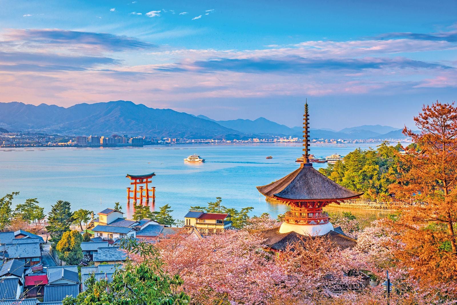 Japanisches Küstenbild mit Torii im Wasser, Kirschblüten und traditioneller Architektur.