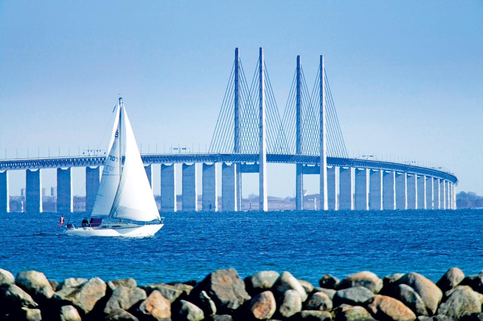 Segelboot vor der Öresundbrücke zwischen Schweden und Dänemark bei blauem Himmel.