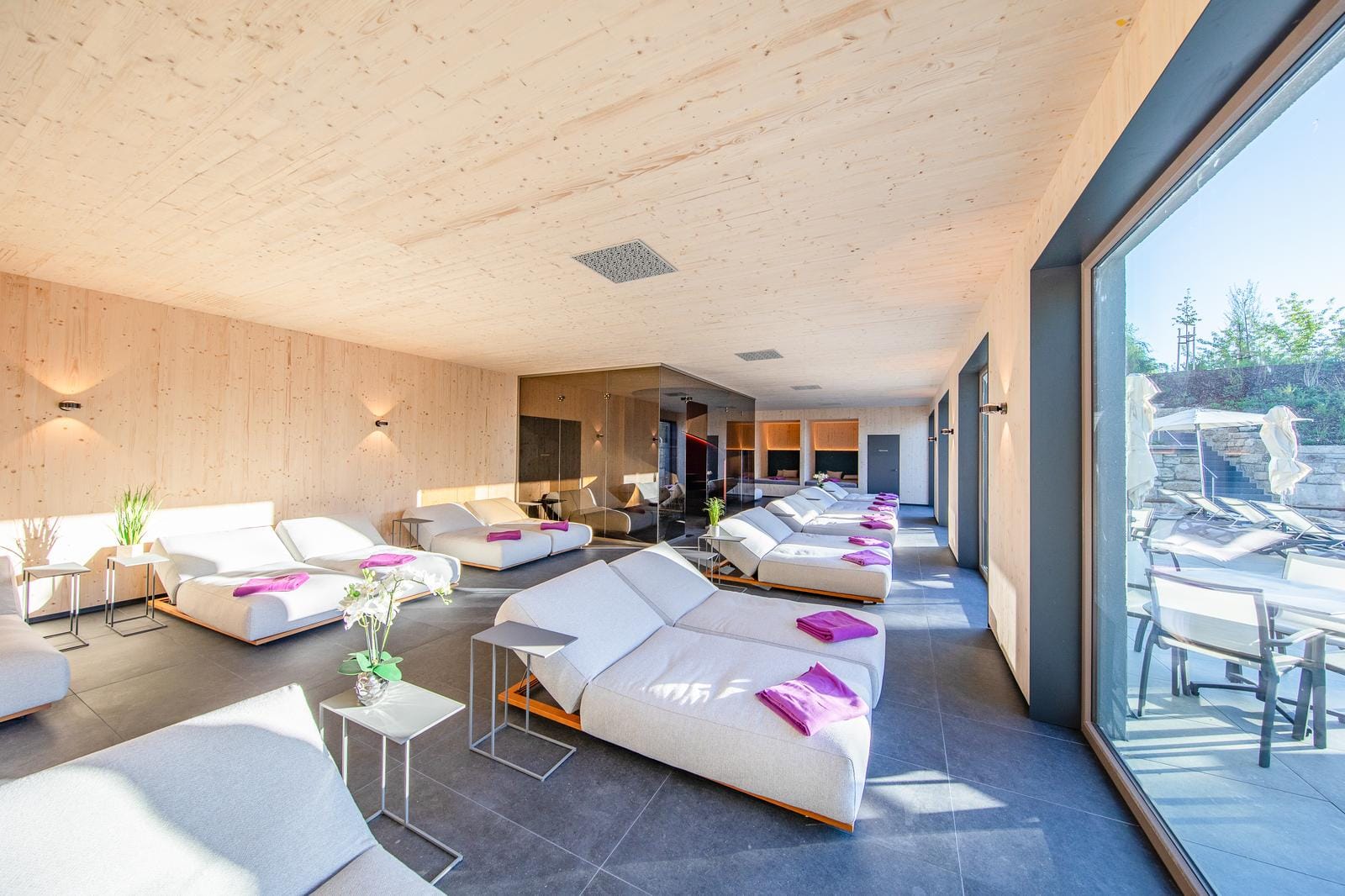 Helles Spa mit Liegen, Holzverkleidung, großen Fenstern und lila Handtüchern.