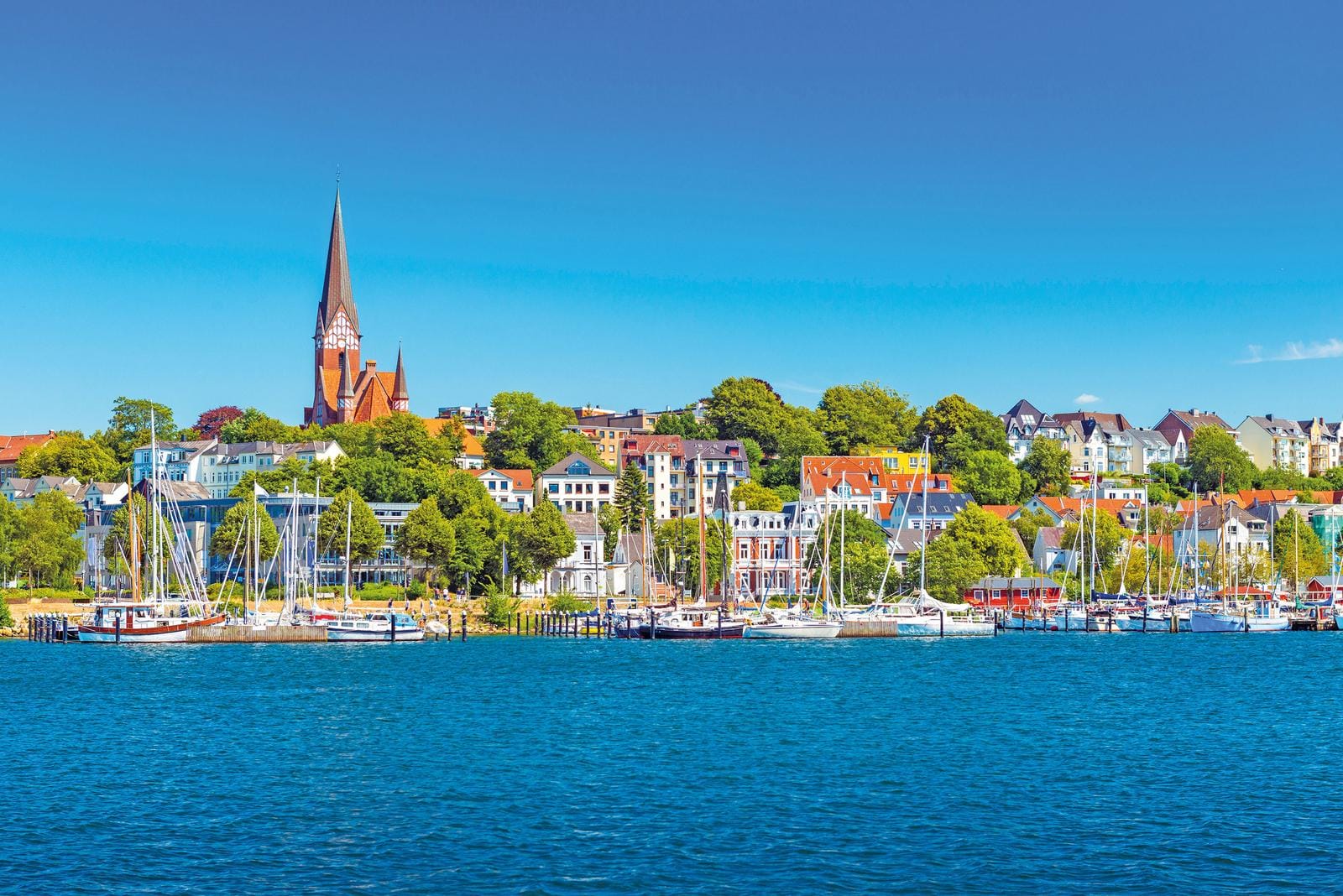 Blick auf Flensburg in Deutschland, mit bunten Häusern und Yachten am Wasser an einem sonnigen Tag.