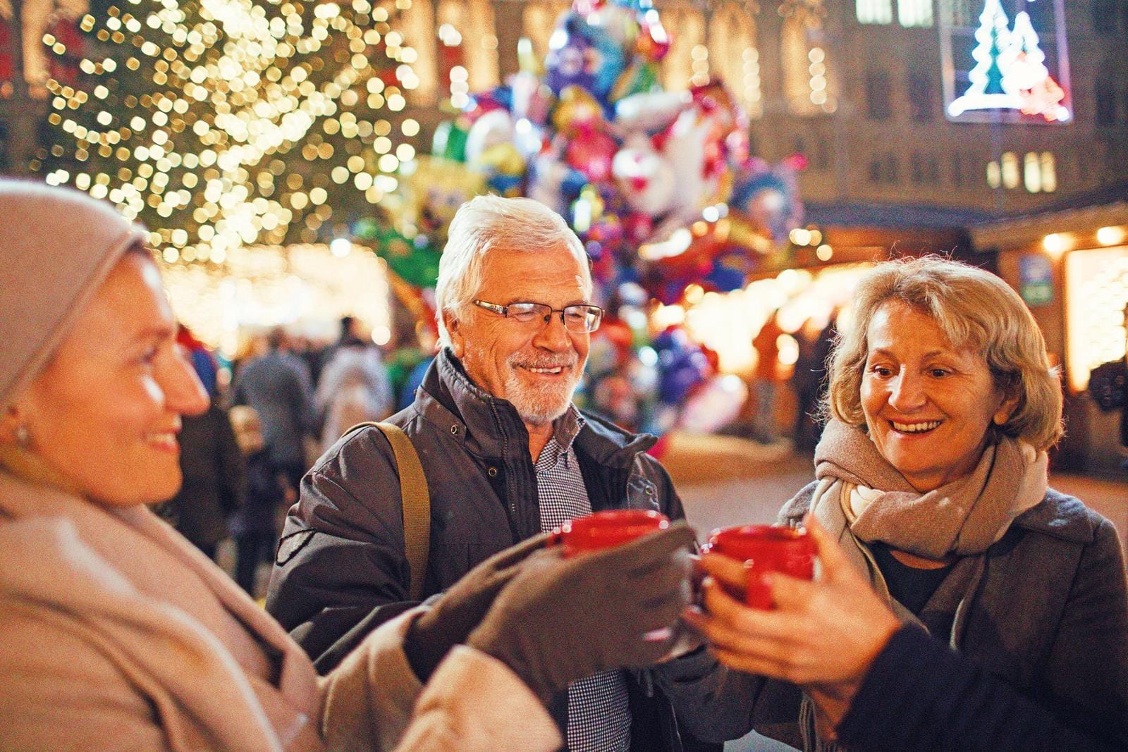 Menschen stoßen mit Tassen auf einem festlichen Weihnachtsmarkt an.