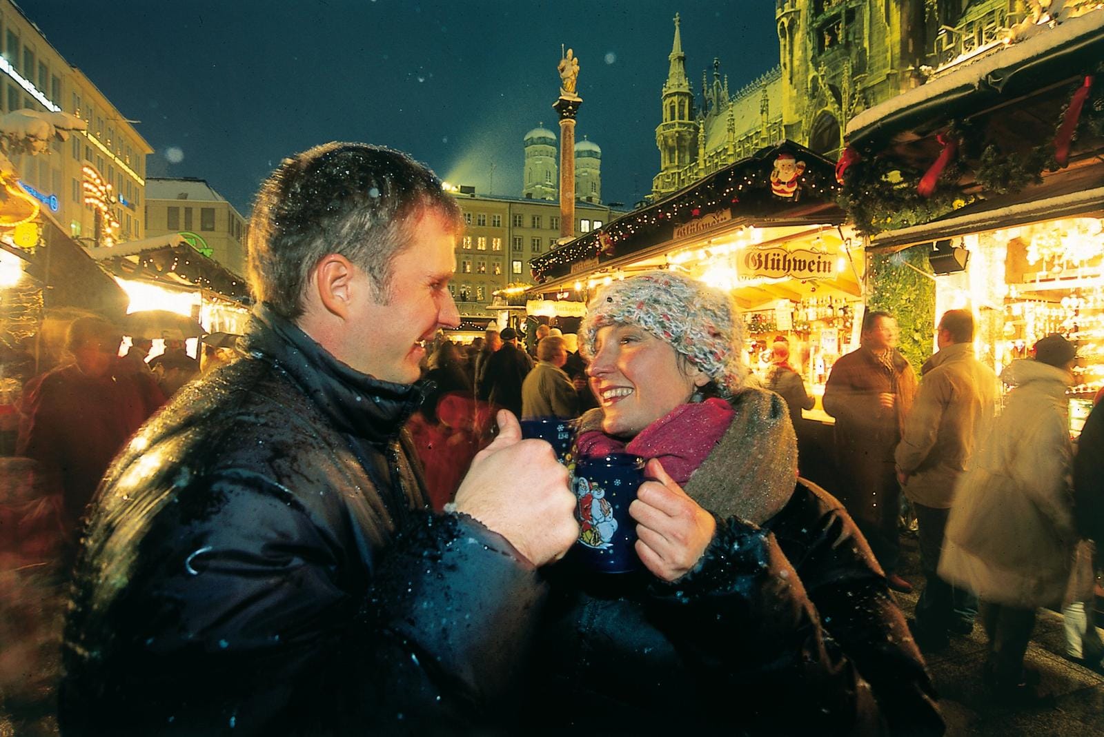 Paar trinkt Glühwein auf Münchner Weihnachtsmarkt, abendliche festliche Atmosphäre.