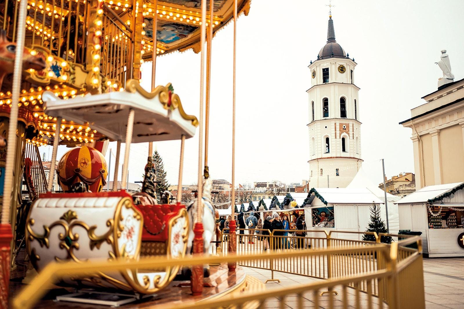 Weihnachtsmarkt in Vilnius, Litauen, mit beleuchtetem Karussell und Kirchturm im Hintergrund.