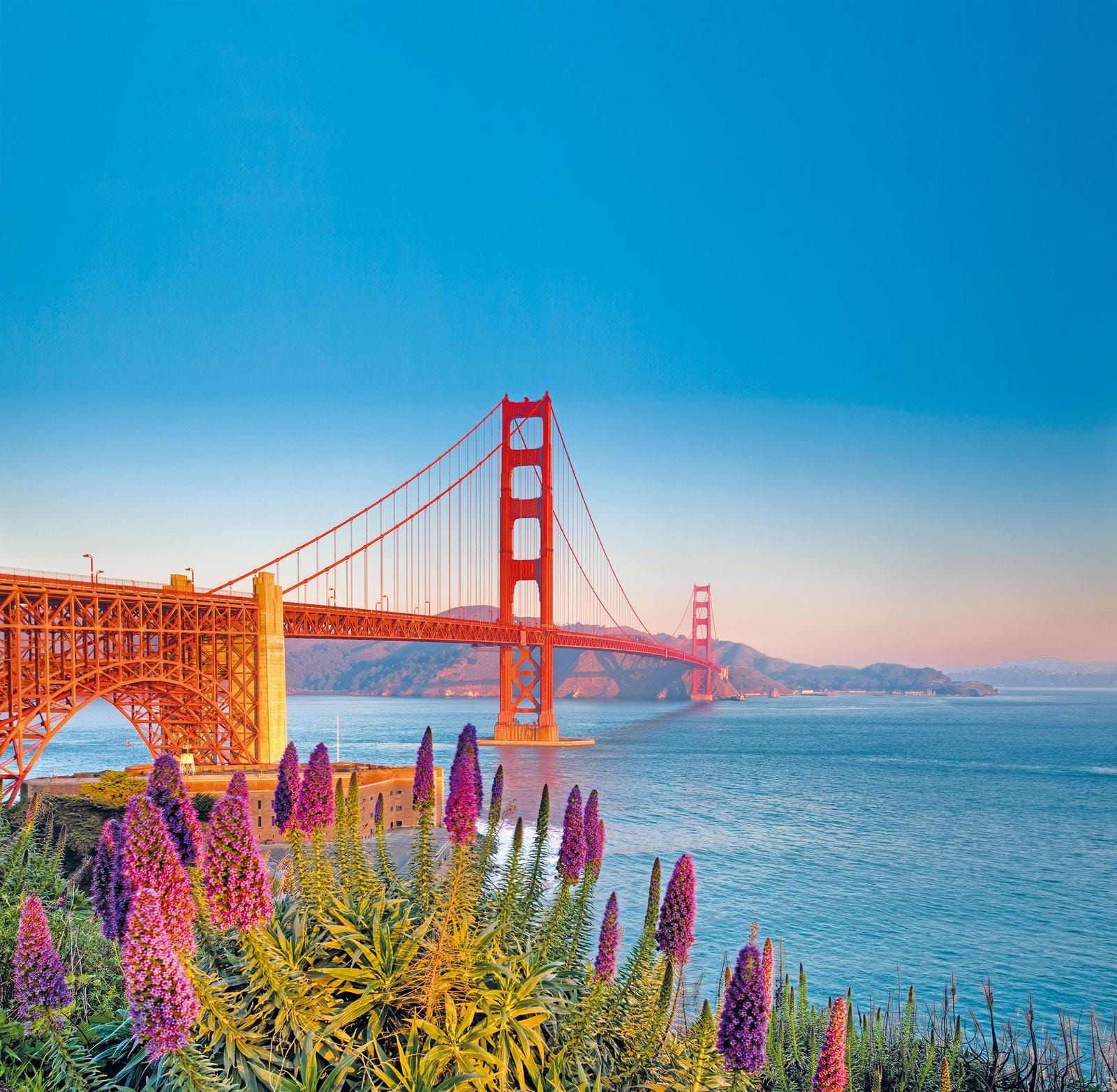 Golden Gate Bridge bei Sonnenuntergang, San Francisco, leuchtend rot über blauem Wasser.