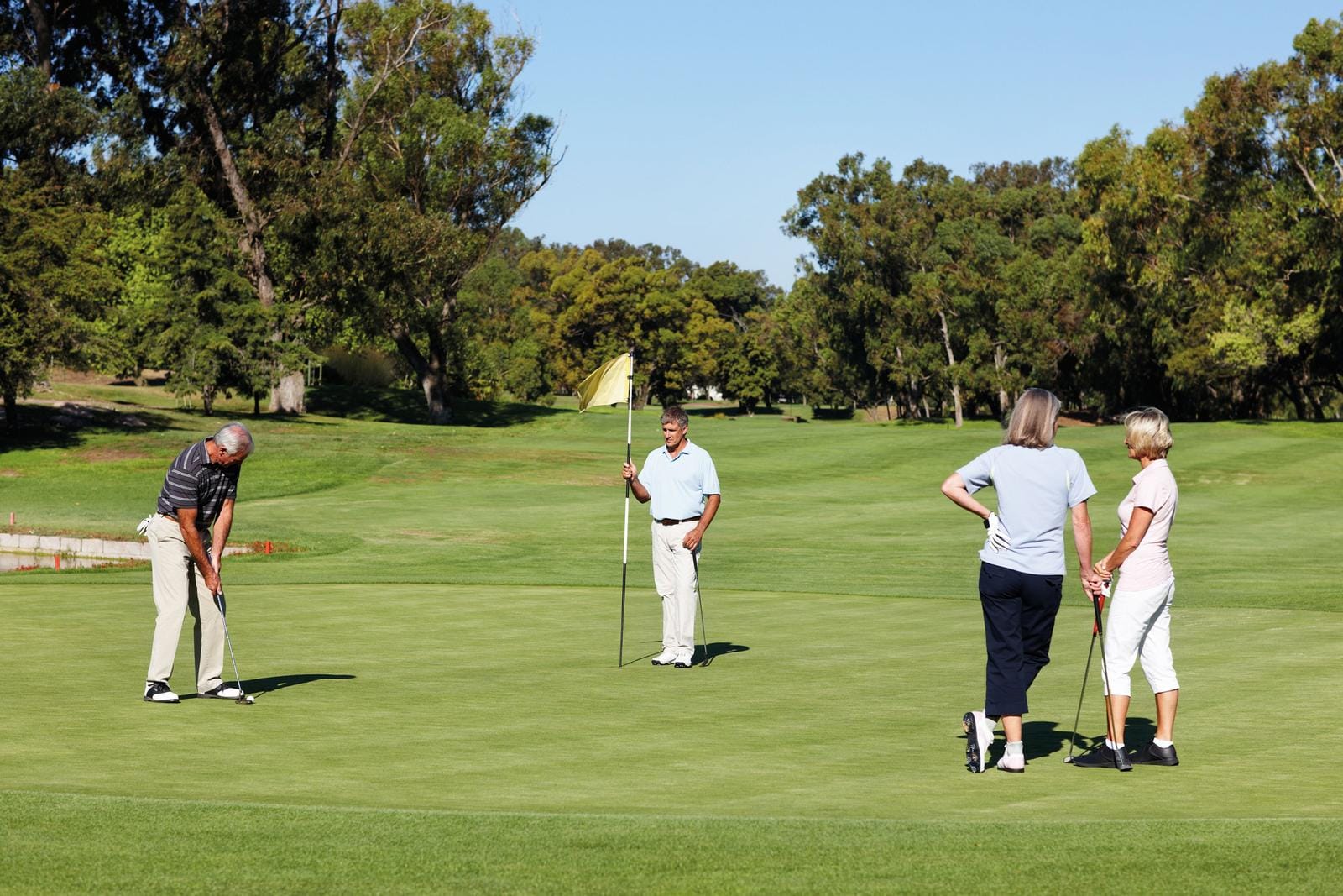 Golfer auf grünem Golfplatz, von Bäumen umgeben, bei sonnigem Wetter.