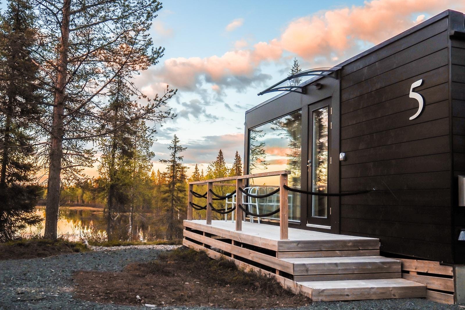 Moderne HĂŒtte in Waldlandschaft, Holzveranda, Abendhimmel mit rosa Wolken.