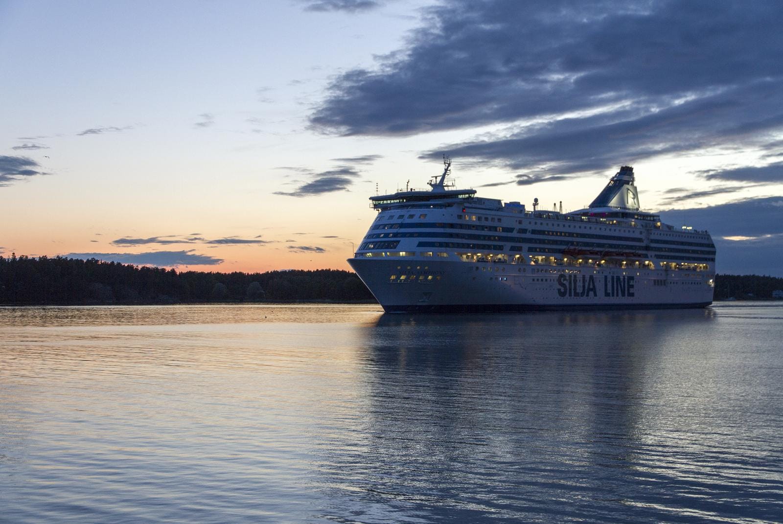 Kreuzfahrtschiff bei Sonnenuntergang auf ruhigem Meer, Himmel in sanften Pastellfarben.