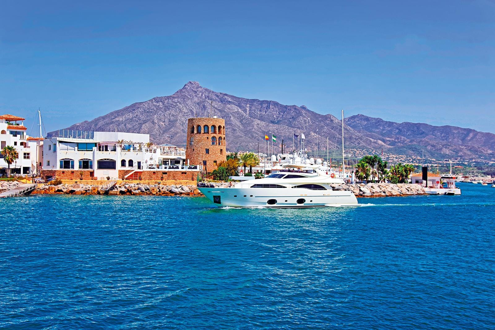 Hafen in Marbella, Spanien mit weißer Yacht und Bergen im Hintergrund bei klarem Himmel.