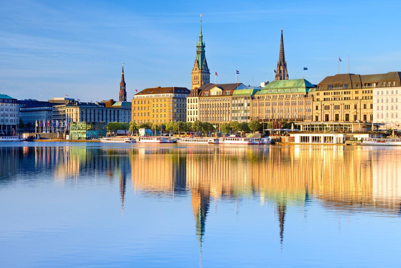 Historische Fassaden am Alsterufer in Hamburg, reflektiert im ruhigen Wasser.