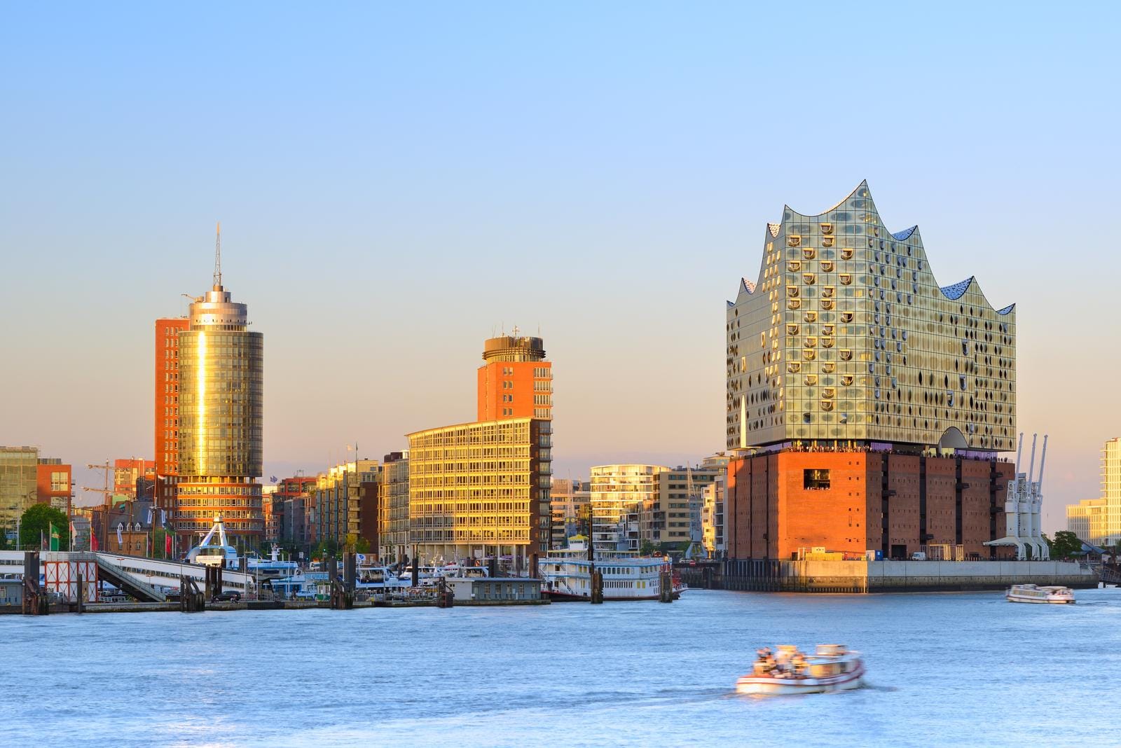 Hamburgs Hafen mit Elbphilharmonie bei Sonnenuntergang, klarer Himmel, Boote im Wasser.