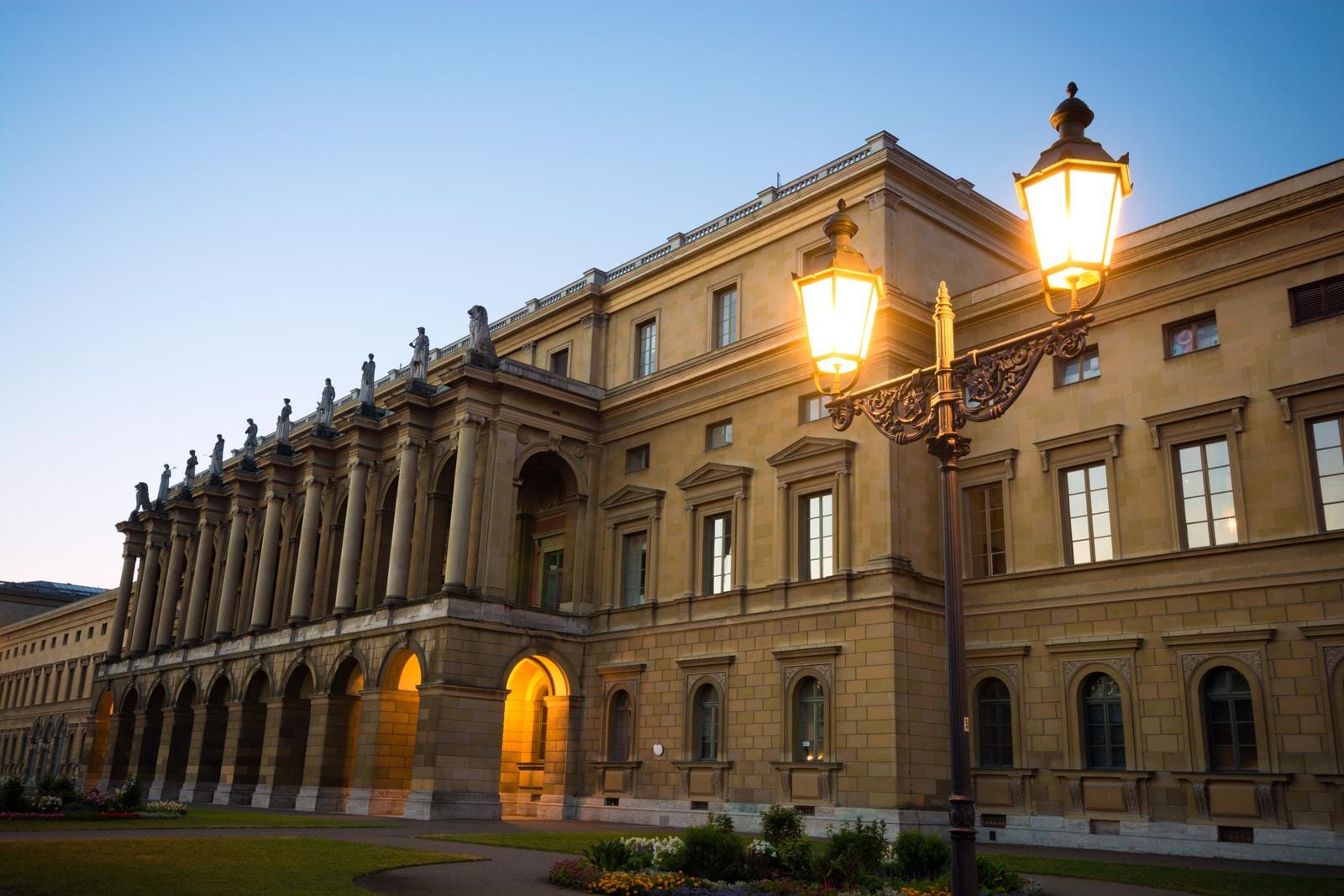 Neoklassizistisches Gebäude in München bei Abenddämmerung, erleuchtet von Straßenlampen.