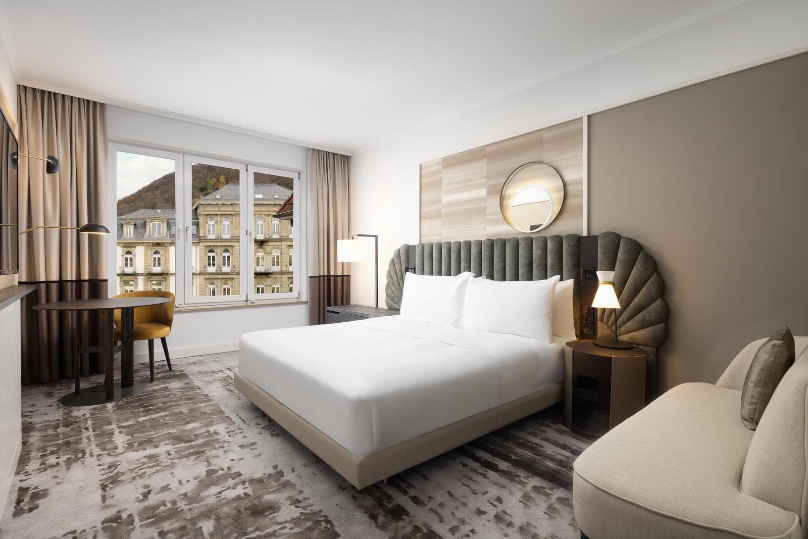 Helles Hotelzimmer mit Kingsize-Bett, modernem Stil und Blick auf historische Gebäude.