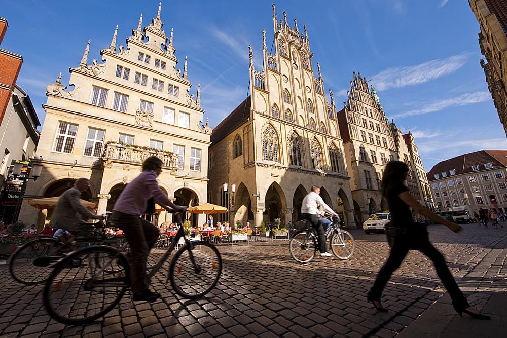 Historische Altstadt Münster, Deutschland, mit gotischen Gebäuden und Radfahrern im Sonnenlicht.