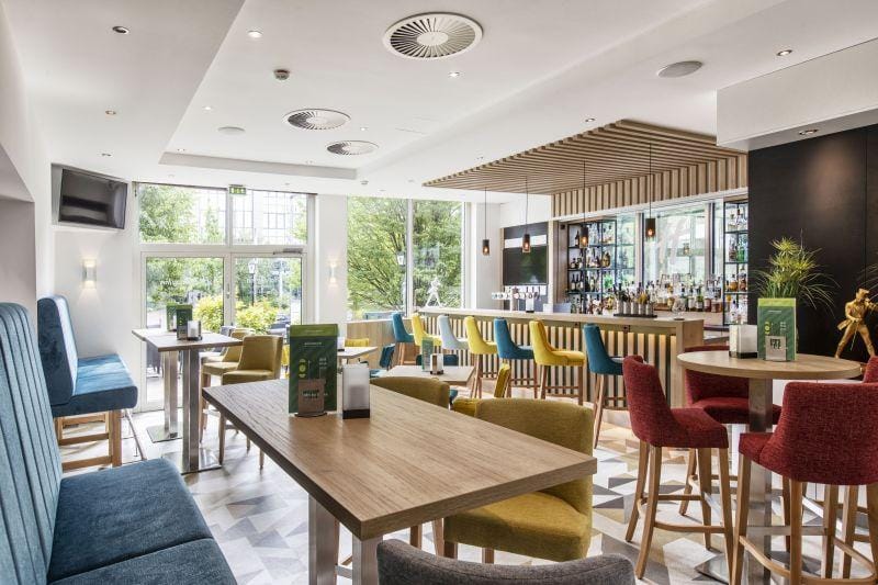 Helle Hotelbar mit bunten Stühlen, modernen Möbeln und Blick ins Grüne.