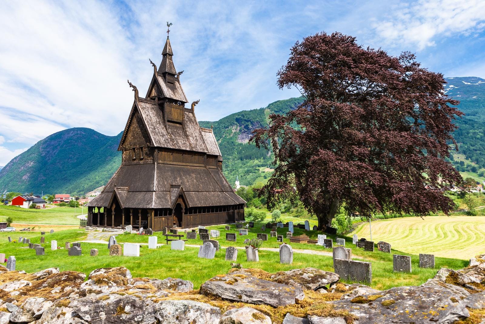 Außergewöhnliche, spitze Kirche neben einem Baum und Gräbern im Grünen