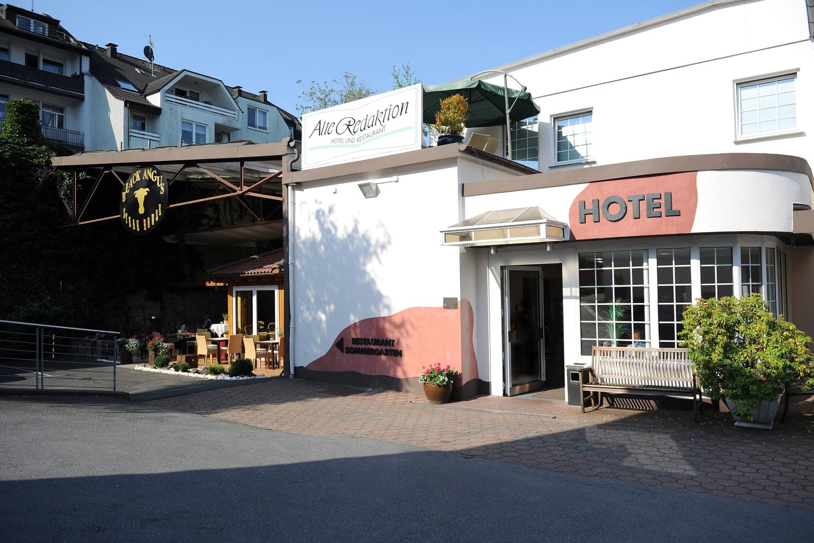Hotel "Alte Redaktion" mit Terrasse, weißer Fassade, roten Akzenten; sonnige Atmosphäre.