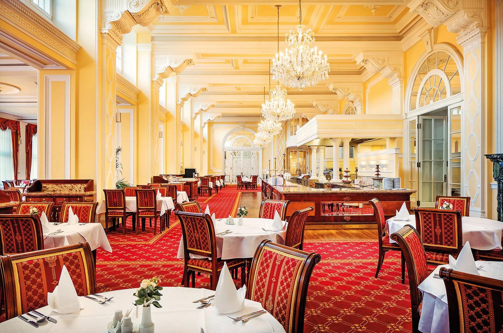 Elegantes Hotelrestaurant mit Kronleuchtern, roten Teppichen und klassischen Holzmöbeln.