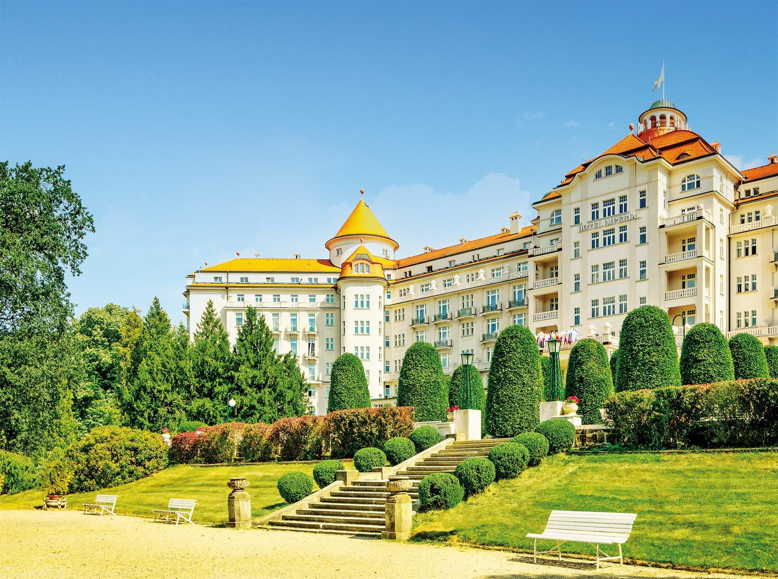 Großes elegantes Hotel mit orangen Dächern, umgeben von gepflegtem Garten.