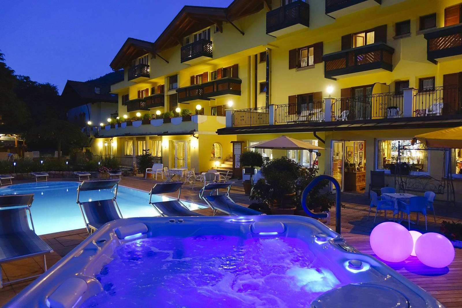 Gelbes Hotel bei Nacht, Pool und beleuchteter Whirlpool, entspannte Atmosphäre.