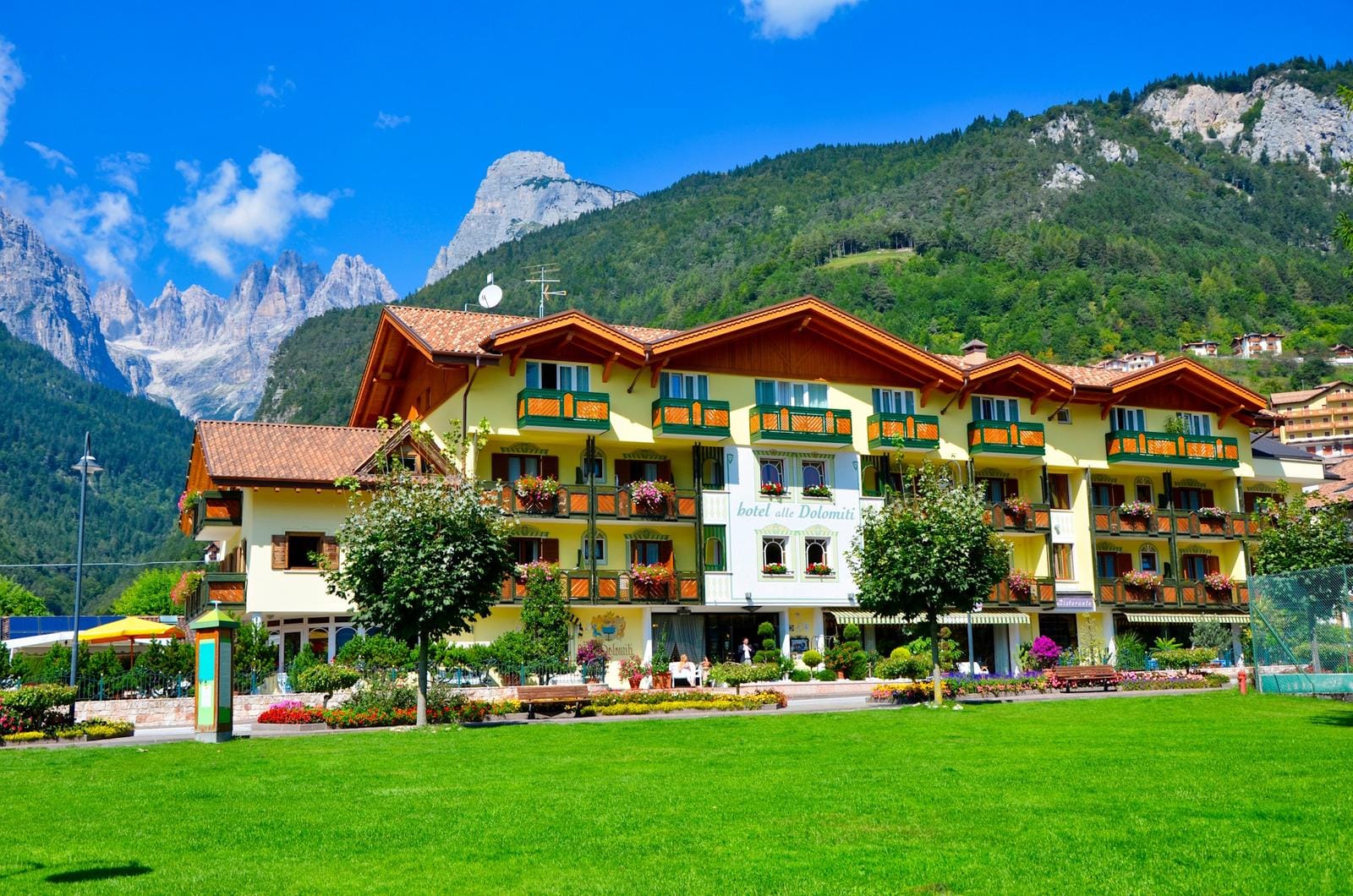 Gemütliches Berghotel in den Alpen, mit Balkon, blühenden Blumen und grünen Wiesen.