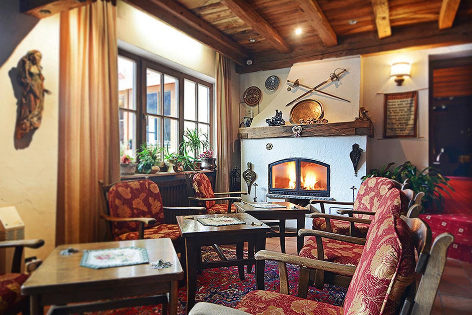 Gemütlicher rustikaler Lounge-Bereich mit Kamin, Holzbalkendecke und roten Polstersesseln.