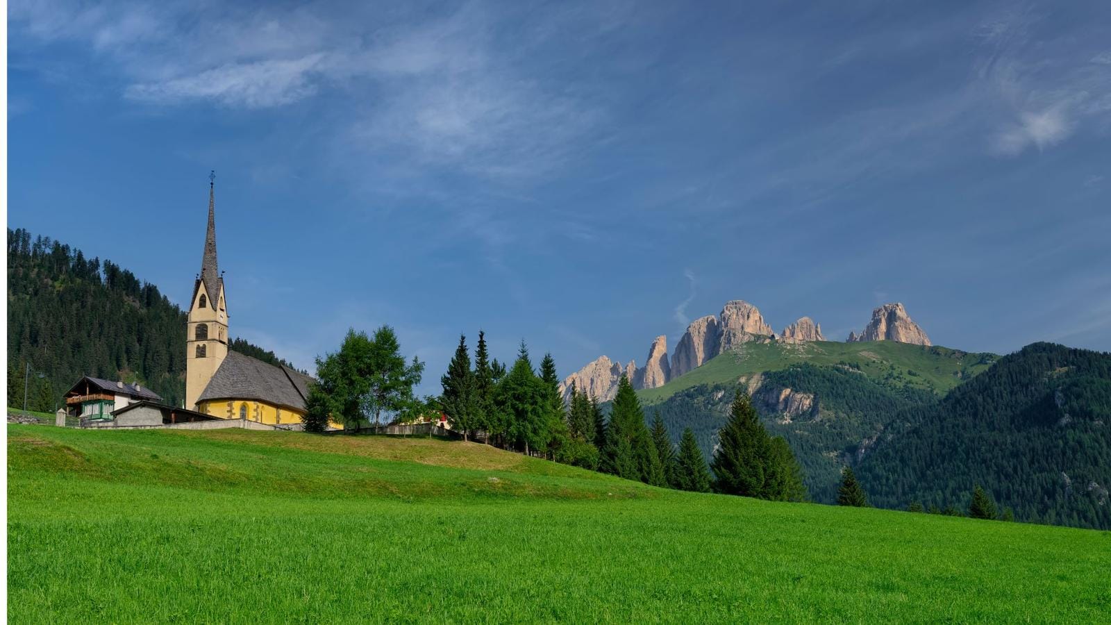 Kirche vor den Dolomiten, Italien; grüne Wiese, blauer Himmel, malerische Berge.