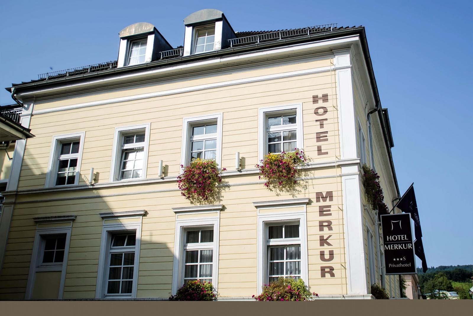 Gelbes Hotel mit Blumenkästen, blauer Himmel, klassischer Stil.