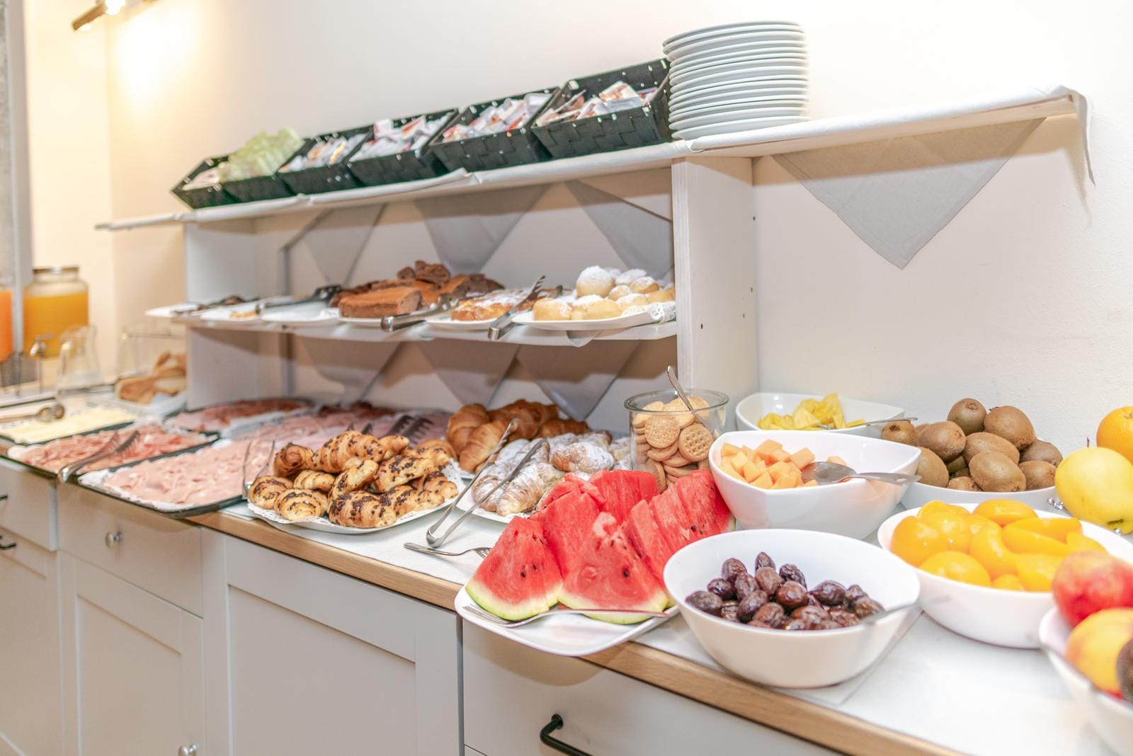 Helles Hotelbuffet mit Gebäck, Aufschnitt, frischem Obst und Säften in warmem Ambiente.