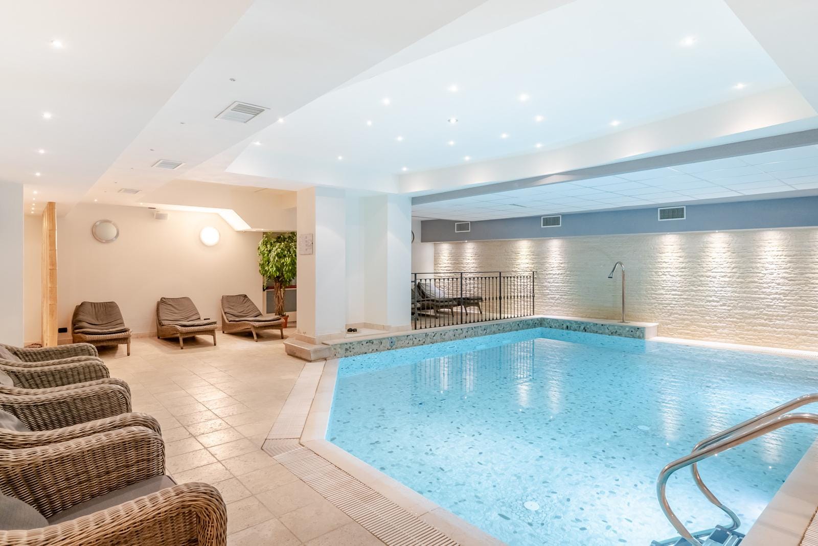 Helles Hotel-Spa mit Innenpool, eleganten Liegen und Steinwänden.