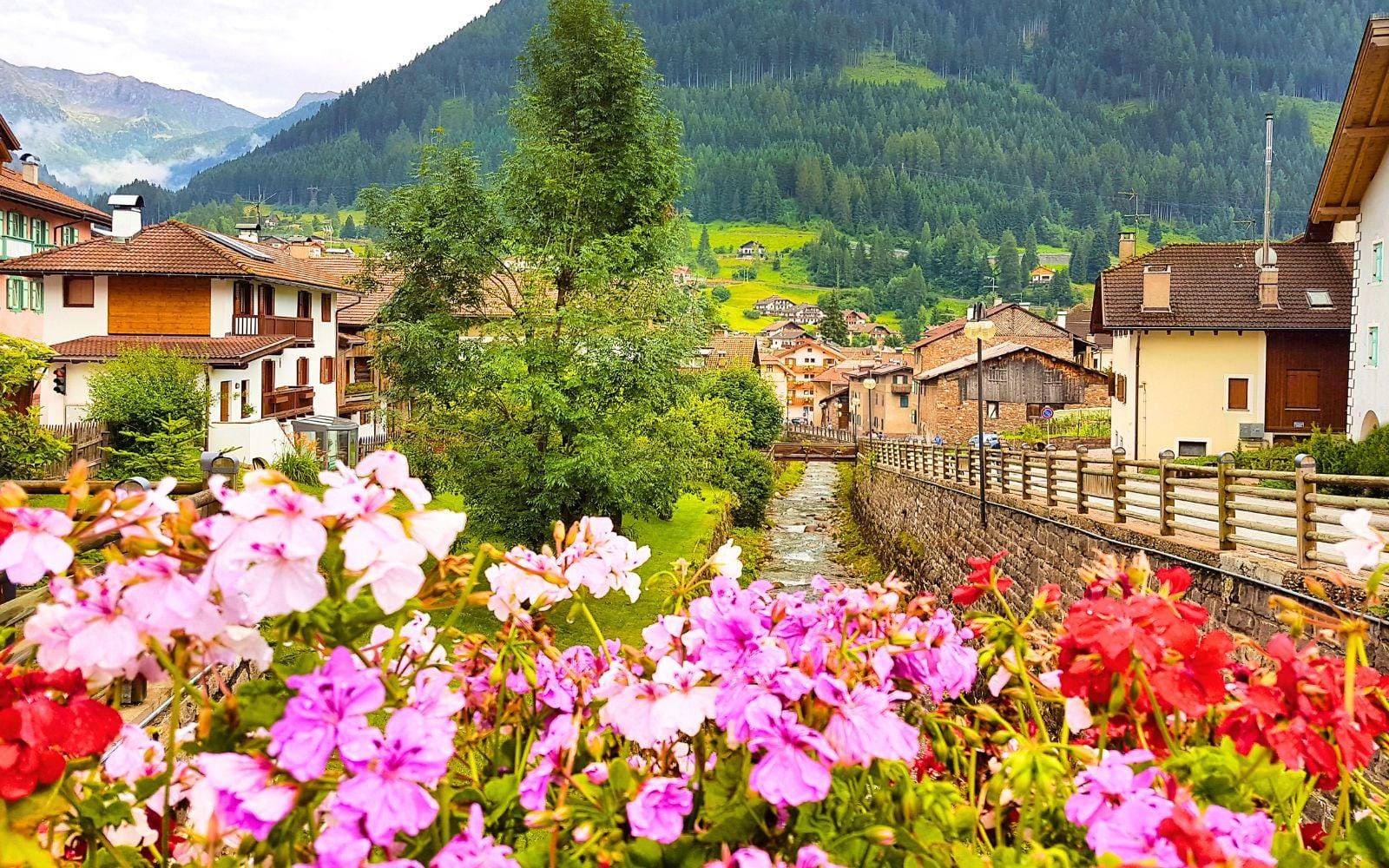 Bunte Blumen vor einem Flusslauf in einem idyllischen alpenländischen Dorf.