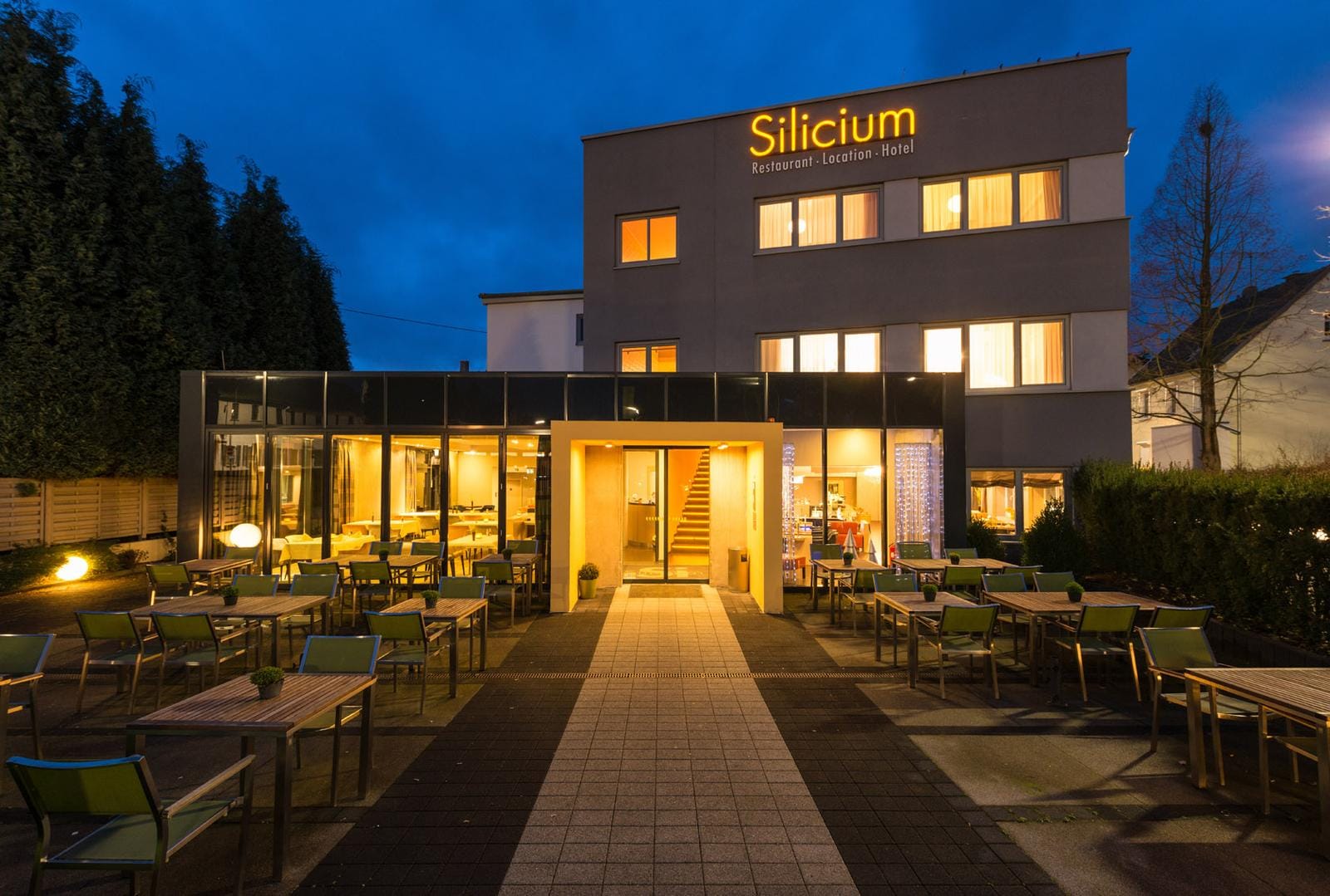 Modernes Hotel mit Glasfassade und gemütlicher Terrasse in warmem Abendlicht.