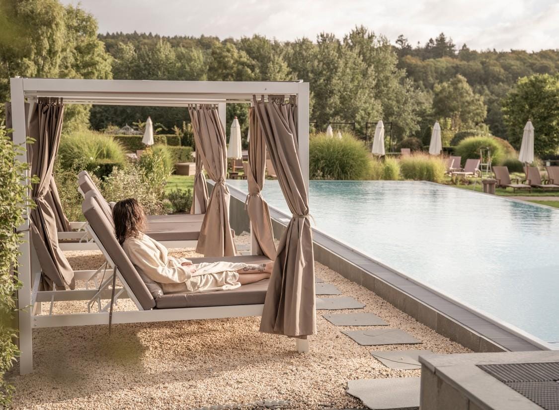 Luxuriöse Pool-Lounge mit Liegen und Pavillons, umgeben von üppigem Grün.