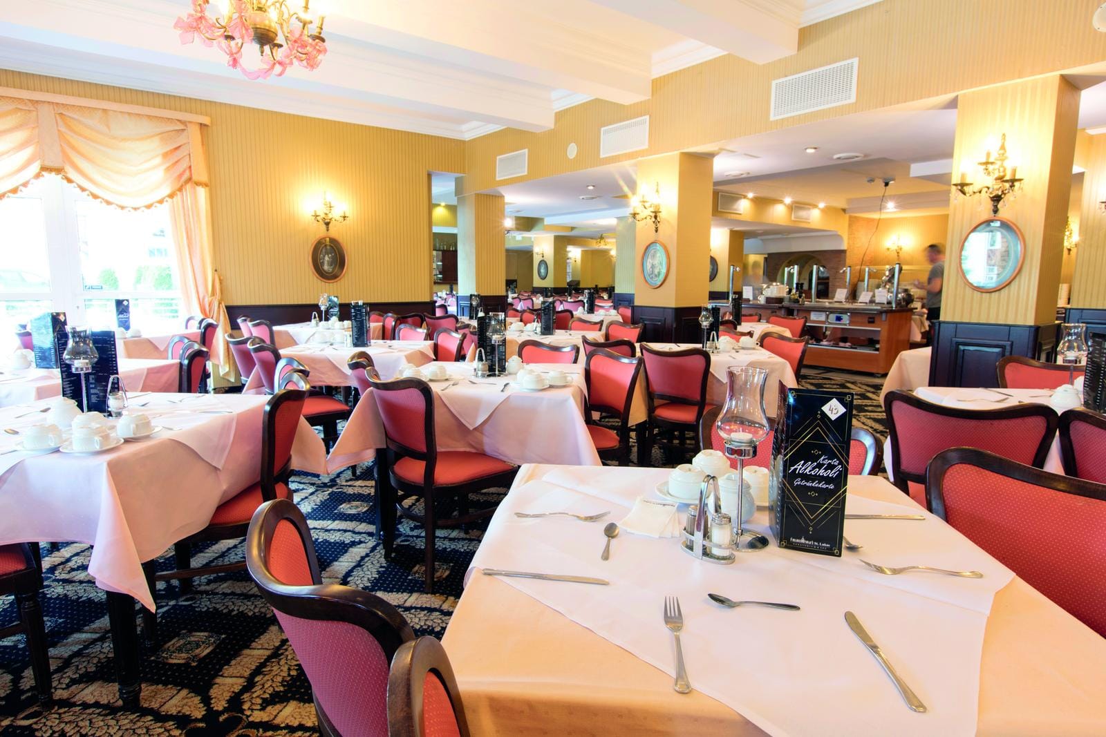 Elegantes Hotelrestaurant mit rosa Stühlen, weißen Tischdecken und goldenen Wänden.