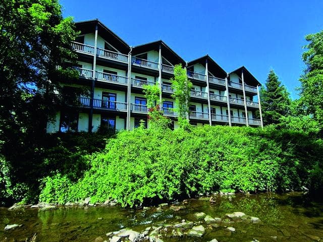 Hotel im traditionellen Stil mit Balkonen, von Bäumen umgeben, neben einem Fluss.