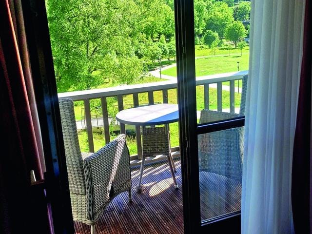 Balkon mit Rattanmöbeln und Blick auf grünen Park bei Sonnenschein.