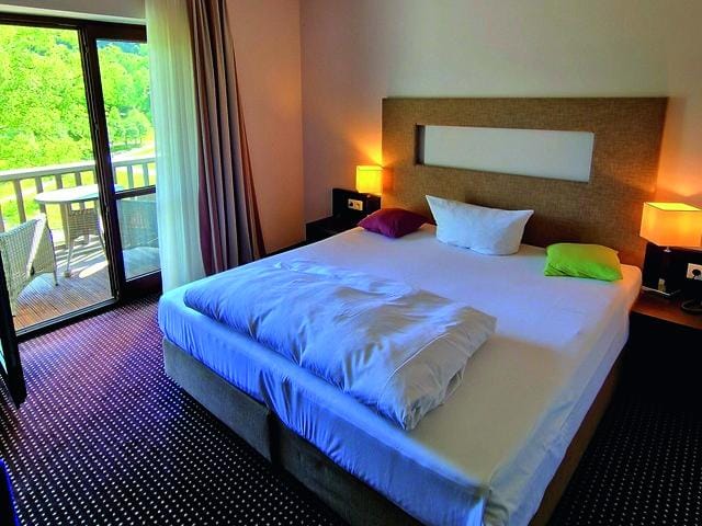 Doppelzimmer mit Balkon, modernem Stil, farbigen Kissen und warmem Licht.