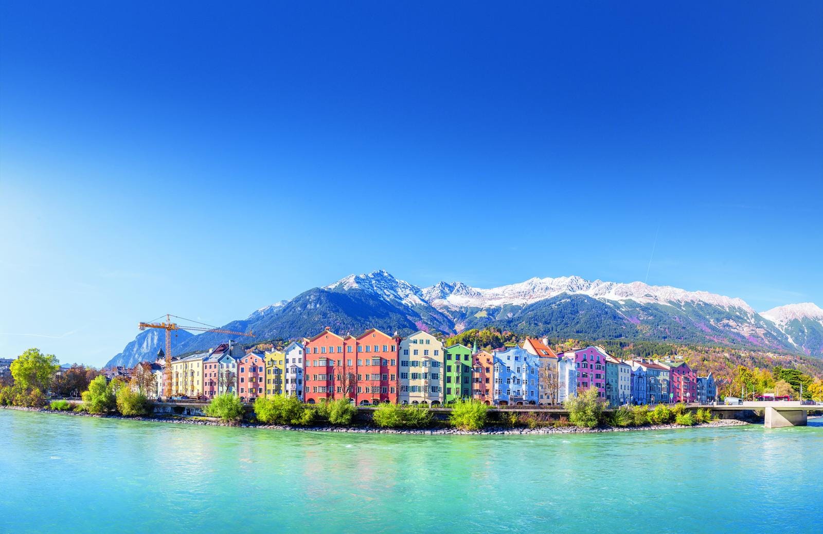 Bunte Häuserreihe am Ufer in Innsbruck, Tirol, vor schneebedeckten Alpenbergen.