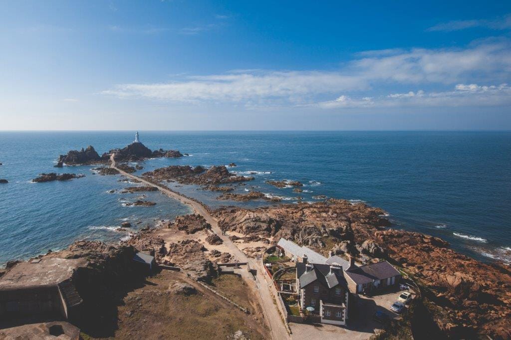 Felsiger Küstenpfad zu einem Leuchtturm, umgeben von blauem Meer und klarer Himmel.
