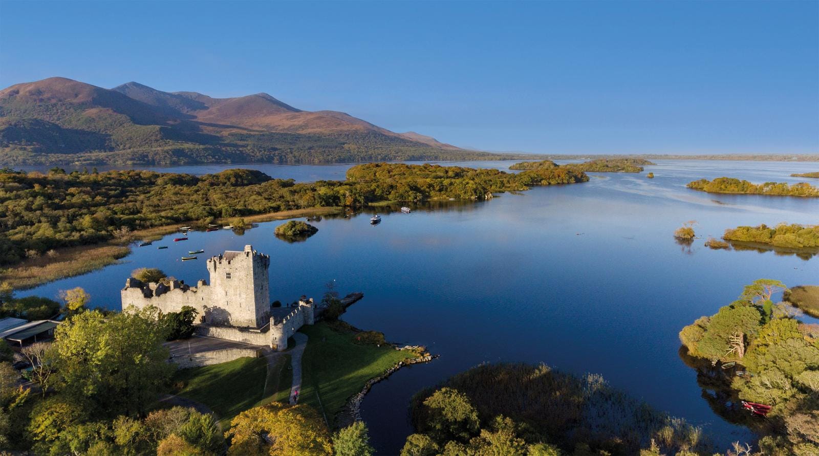Irland, Killarney. Ross Castle am Lough Leane mit Bergkulisse und blauem Himmel.