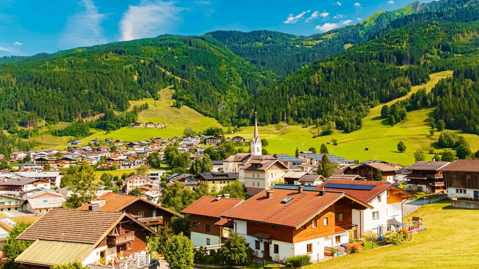 Idyllisches Dorf in Tirol, Österreich mit Kirche, umgeben von grünen Hügeln und Bergen.